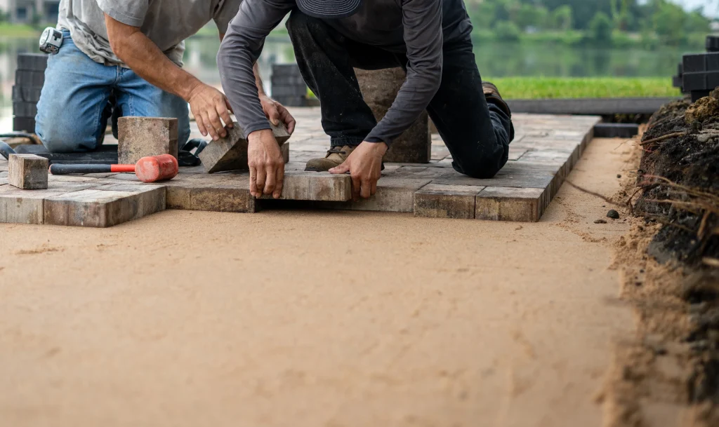 Two landscapers laying paver blocks together